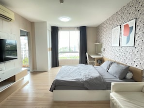 A modern hotel room with a bed, a desk, a TV, and a balcony with curtains. - Room117atchangwattana (Pak Kret)