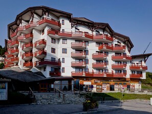 Ein mehrstöckiges Hotel mit Balkonen, einem Restaurant und einer Seilbahn im Hintergrund.