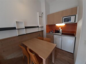 Eine kleine Küche mit Mikrowelle, Toaster und Spüle. Ein Holztisch und Stühle stehen bereit.