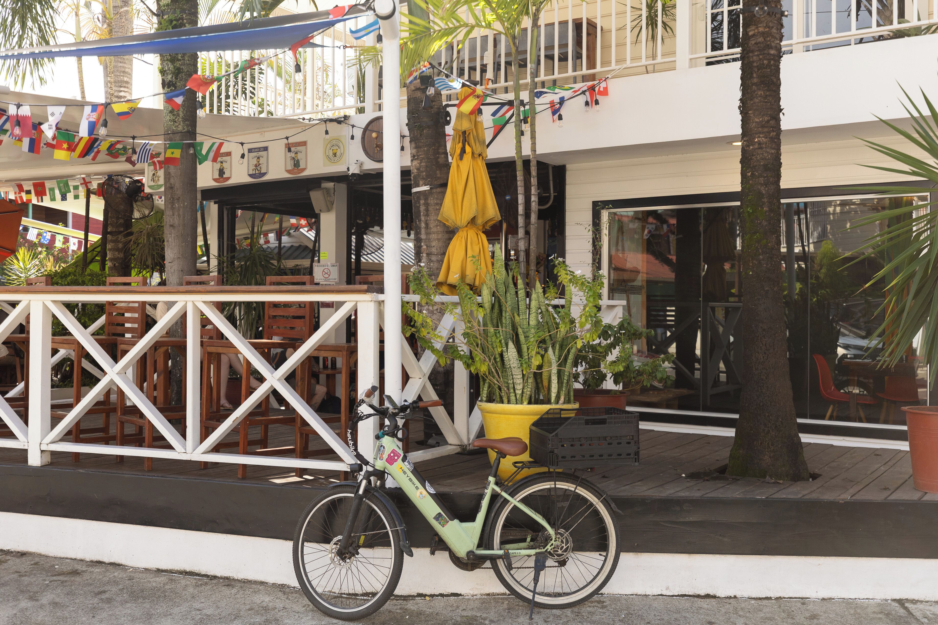 Una bicicleta estacionada frente a un edificio de fachada blanca, un paraguas amarillo y un cartel que prohíbe perros.