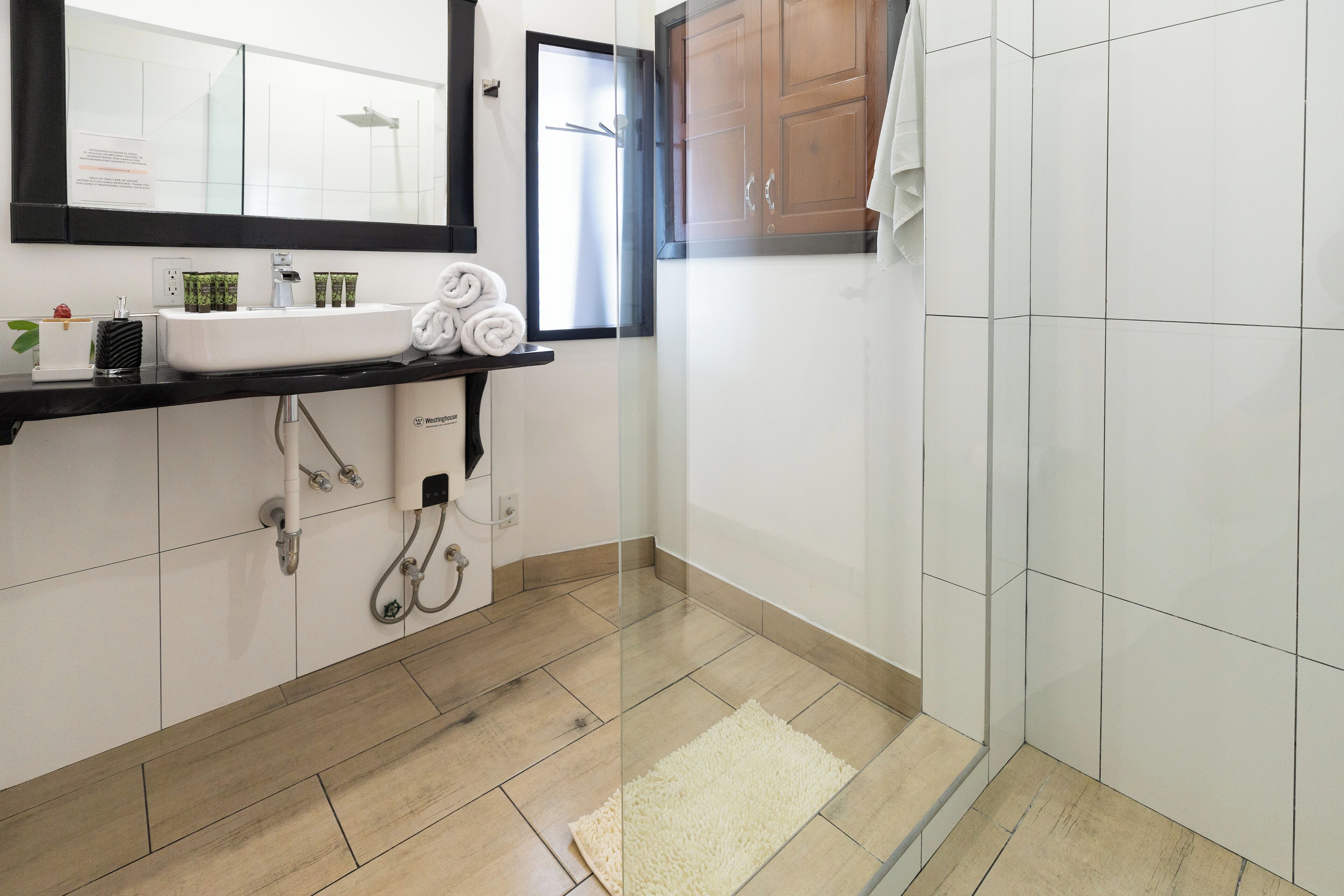 Une salle de bain avec un lavabo blanc, un miroir et un porte-serviettes. Il y a un espace douche avec une porte en verre et une serviette accrochée au mur.