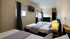 Habitación de hotel con dos camas, un televisor de pantalla plana montado en la pared, un escritorio con lámpara y una ventana con cortinas.