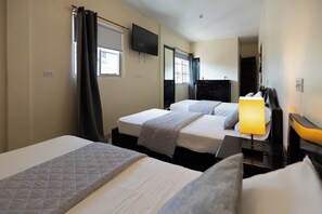 Habitación de hotel con dos camas, un televisor de pantalla plana montado en la pared, un escritorio con lámpara y una ventana con cortinas.