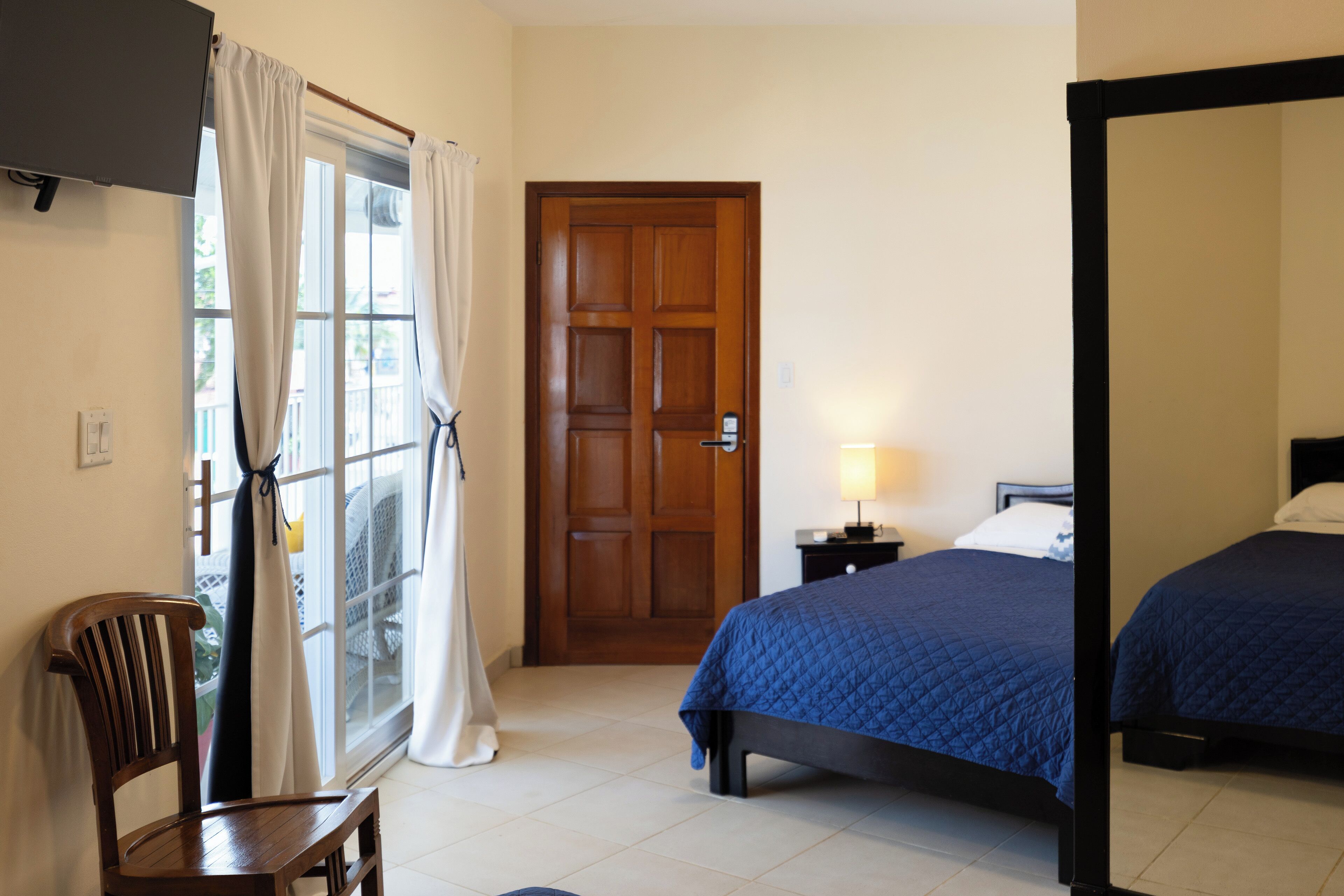 Een kamer met een bed, een stoel, een deur en een raam met gordijnen.