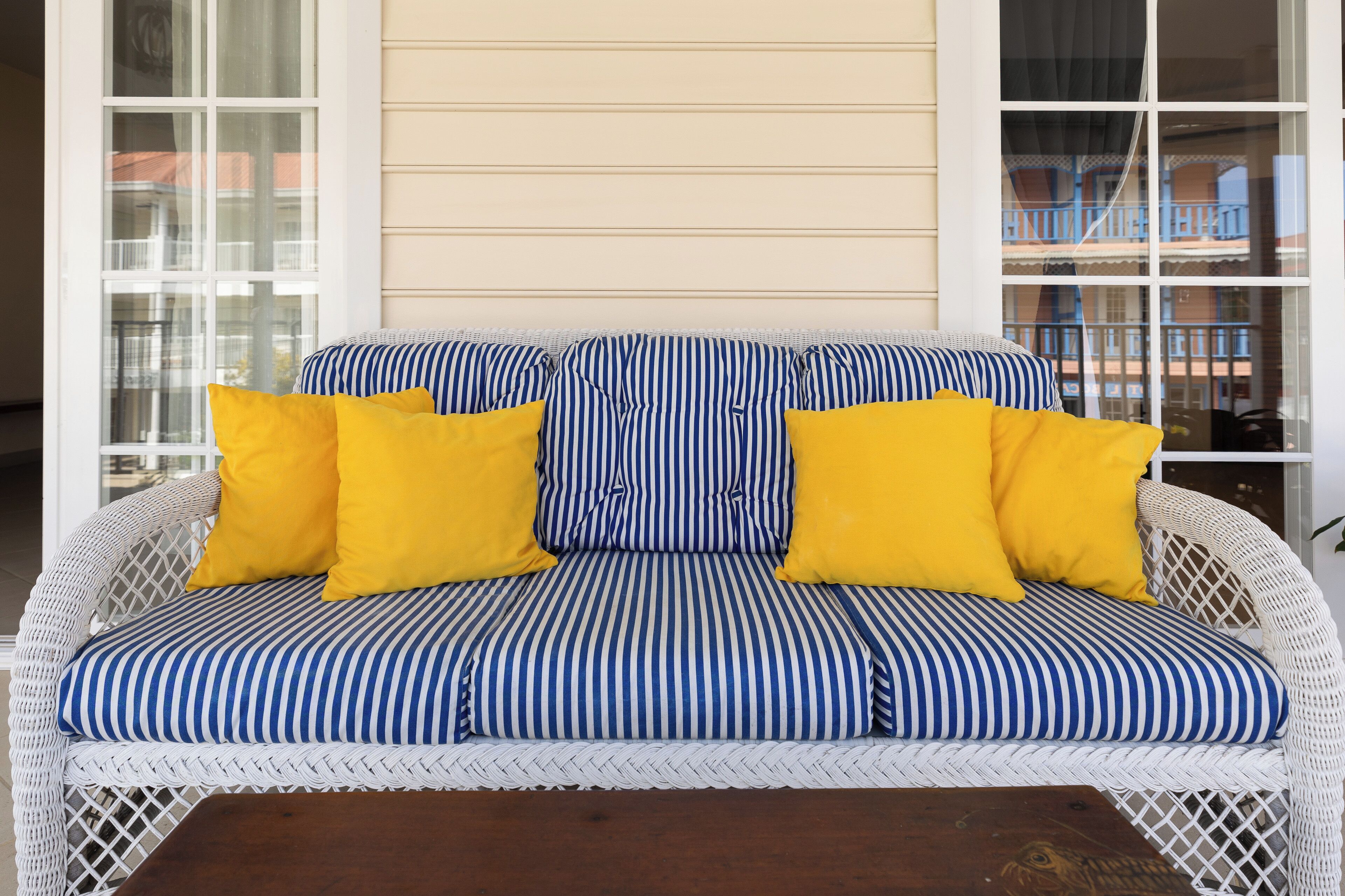 Ein weißes Korbsessel-Sofa mit blau-weißen Streifenpolstern und zwei leuchtend gelben Kissen.