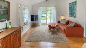 A living room with a wooden floor, a red sofa, a television, a painting, and a window with curtains. - 2 bedroom stunning home in Rørvig (Rørvig)
