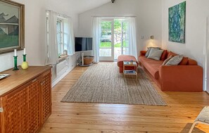 A living room with a wooden floor, a red sofa, a television, a painting, and a window with curtains. - 2 bedroom stunning home in Rørvig (Rørvig)