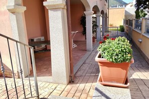 A courtyard with a potted plant, a metal railing, and a building with arches. - Cala Gonone, 3-room apartment, 1st floor (Cala Gonone)