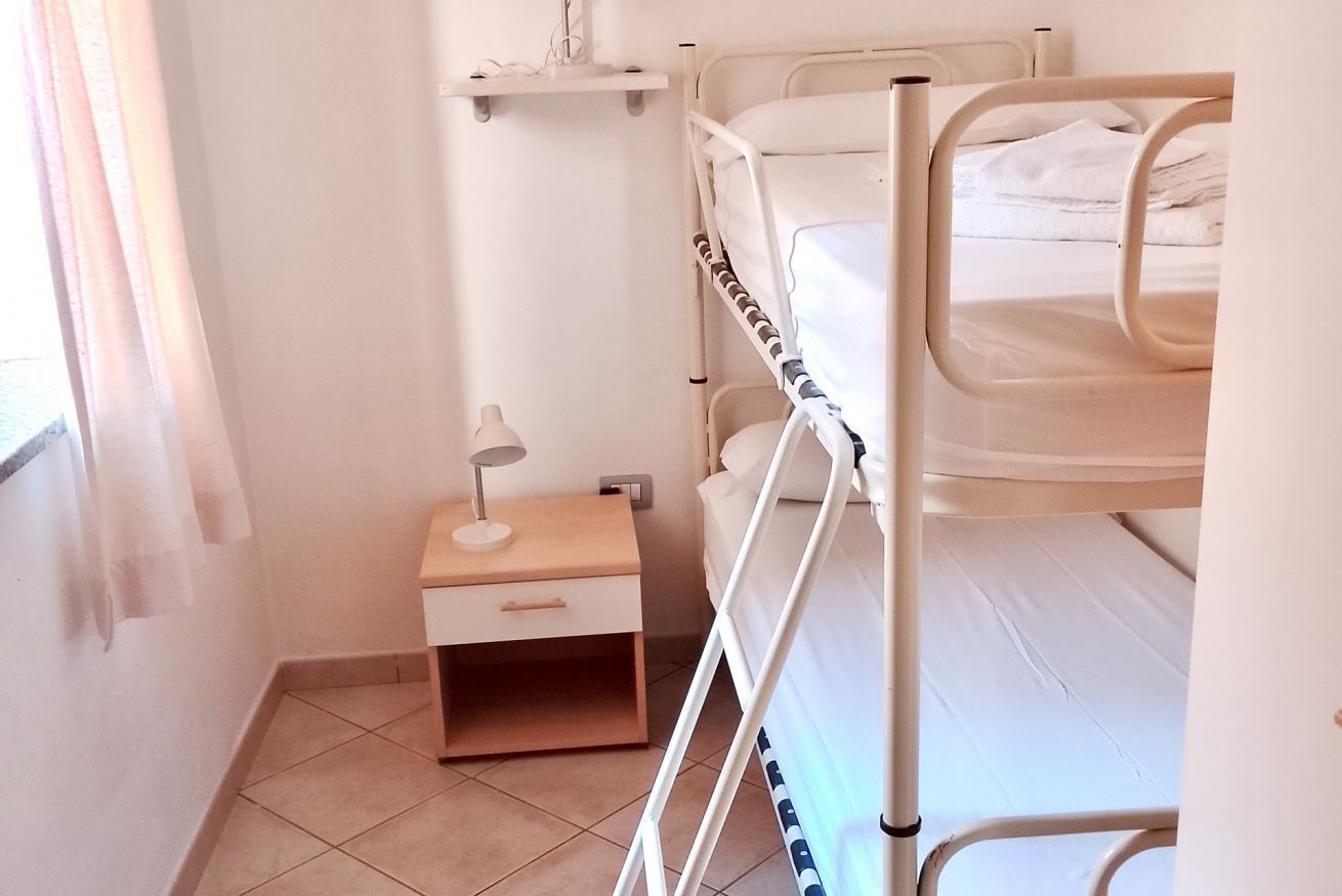 Una camera con un letto a castello, un comodino, una lampada e uno scaffale sopra il letto.
