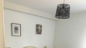 Een slaapkamer met een bed, twee aan de muur bevestigde foto's, een bedlamp en een hangende lamp.