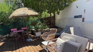 Een houten terras met rieten meubilair, een rieten parasol en een bloempot.