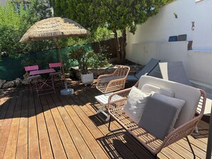 Eine Holzterrasse mit Korbmöbeln, einem Reetdachschirm und einem Blumentopf.