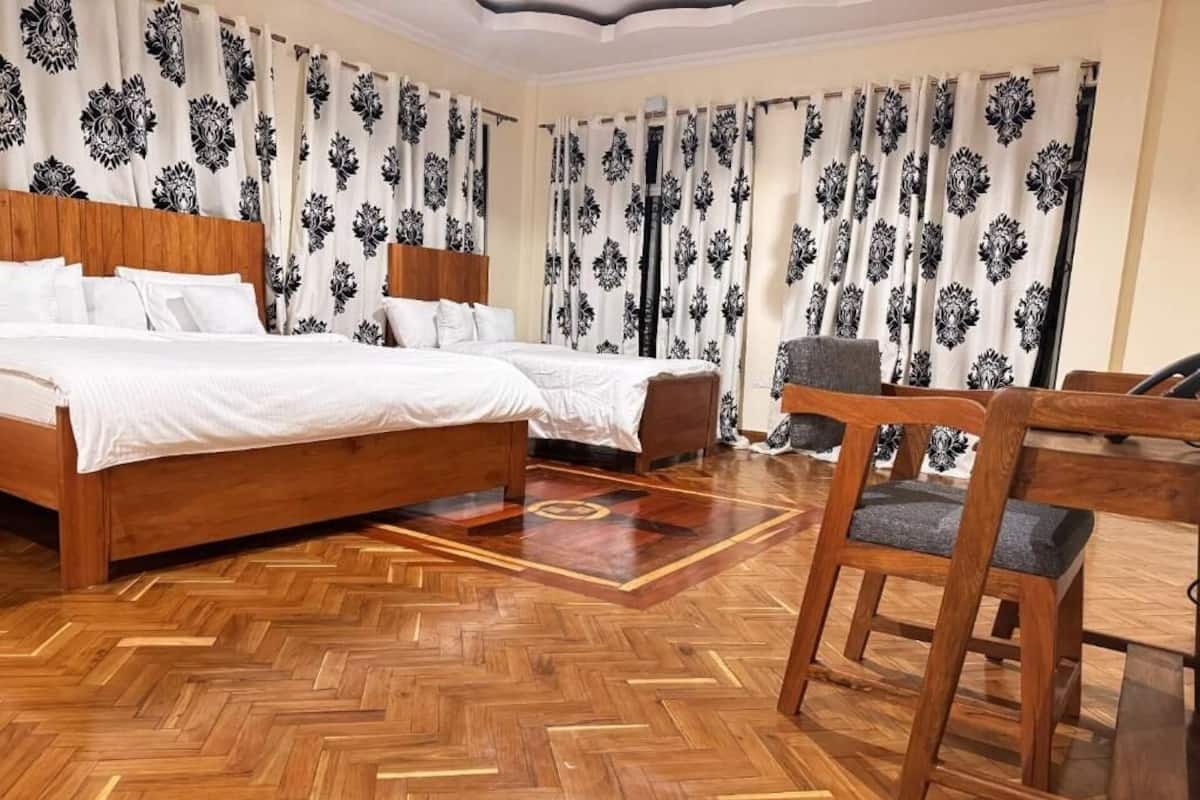 Ein Hotelzimmer mit Holzboden, zwei Betten, einem Sessel und einem Vorhang mit Muster.