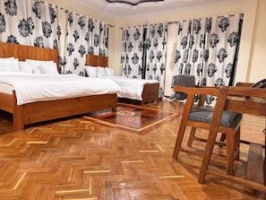 Ein Hotelzimmer mit Holzboden, zwei Betten, einem Sessel und einem Vorhang mit Muster.