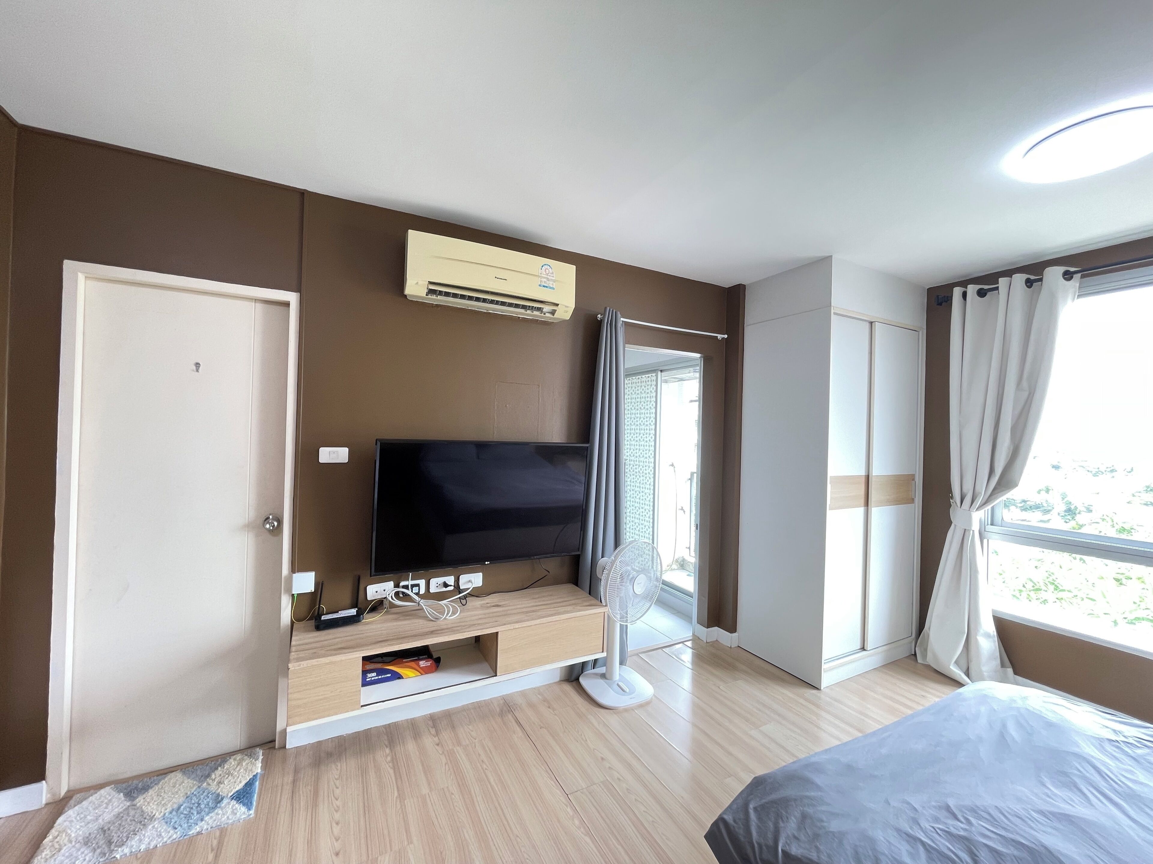 A bedroom with a bed, a TV, a fan, and a window with curtains.
