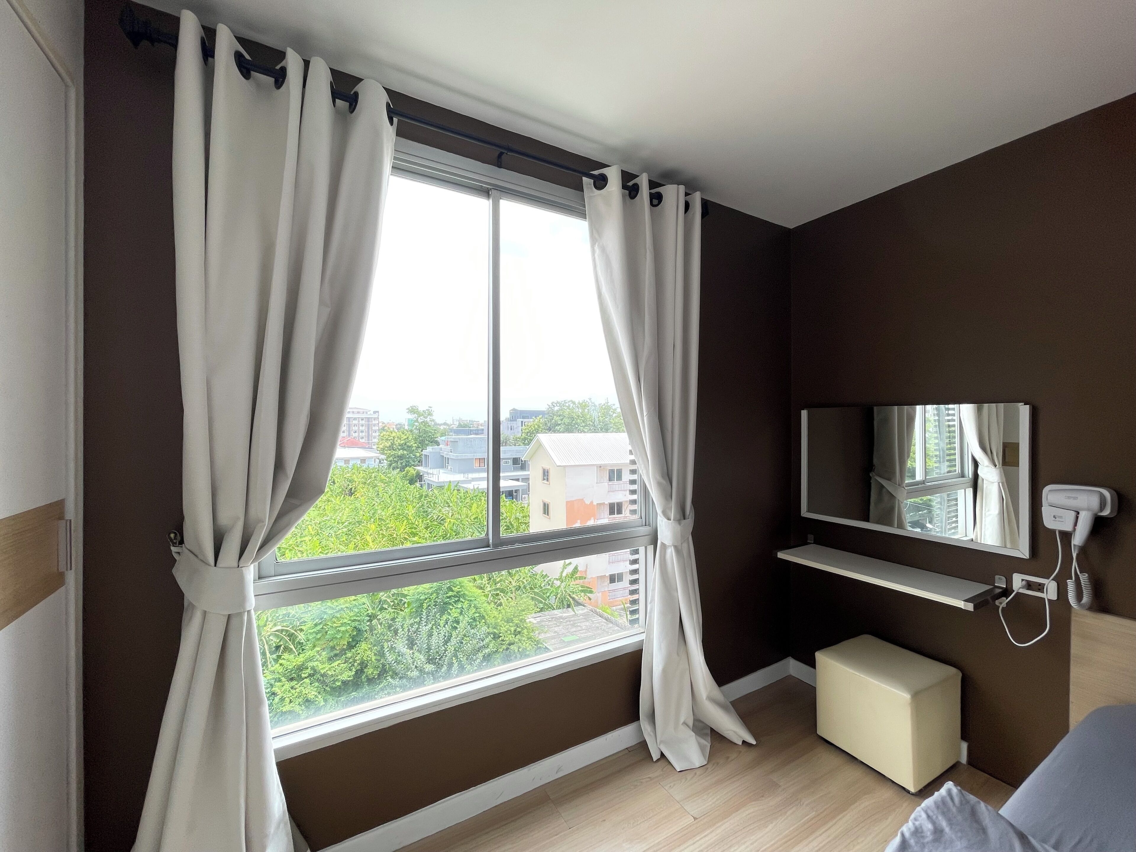 A bedroom with a large window, a bedside table, a mirror, and a TV.