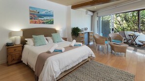 Un dormitorio con cama, mesitas de noche, sillas de mimbre y vista al exterior.