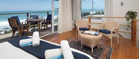 A hotel room with a large bed, a small table, two chairs, a view of the ocean, and a balcony.