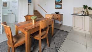 Una mesa de comedor de madera con sillas, una pequeña escalera, una zona de cocina con un fregadero y dos cuadros en la pared.
