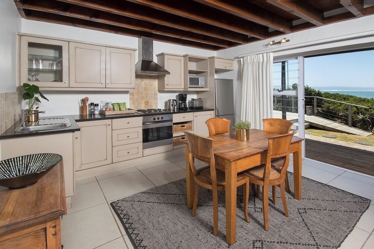 A modern kitchen with a dining area, large windows, and a view of the sea.