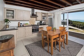 Ett modernt kök med matplats, stora fönster och utsikt över havet.