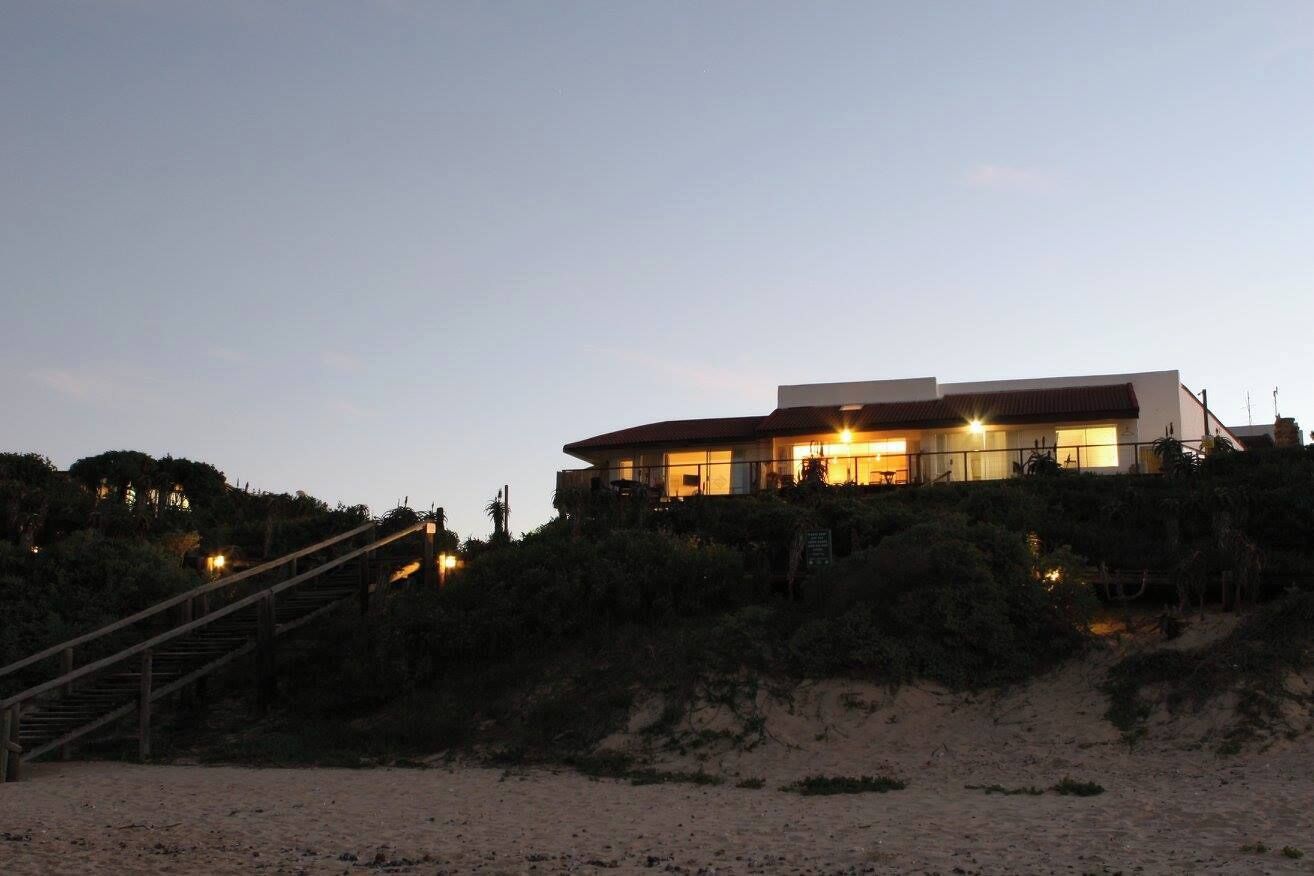 A beachfront property with a curved building, a staircase leading up, and a sandy beach in the foreground.