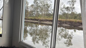 Una habitación con un ventanal grande, una cama y vista a un cuerpo de agua con árboles.