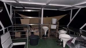 Una cocina con electrodomésticos de acero inoxidable, un bote de basura y repisas con diversos objetos.