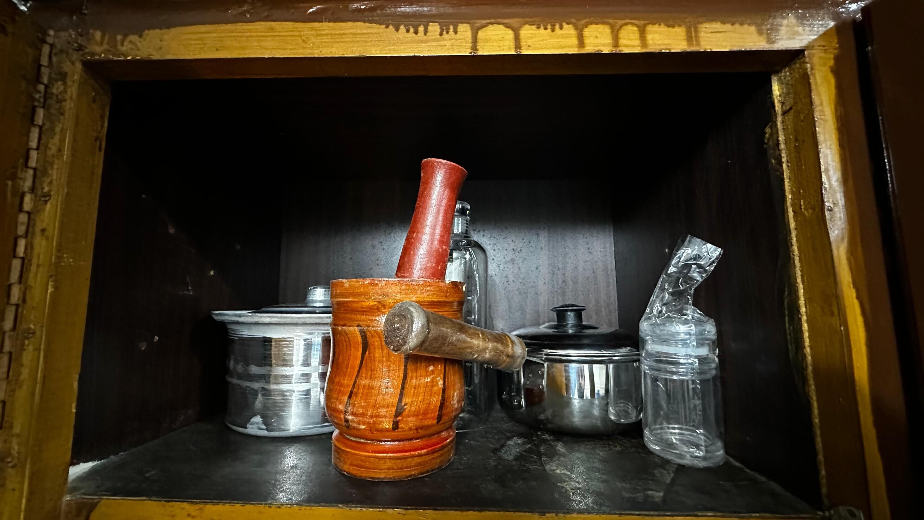 A wooden cabinet with a metal container, a wooden mallet, and a glass bottle.