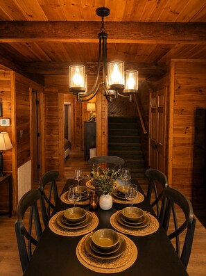 Un interno in legno con un tavolo da pranzo imbandito per sei persone, un lampadario e una scala.