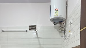 Een badkamer met gestreepte tegels, een handdoekhouder, een rode emmer en een boiler.