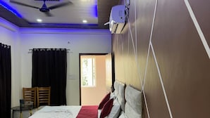 Een hotelkamer met twee bedden, een plafondventilator, een airconditioning en een raam met gordijnen.