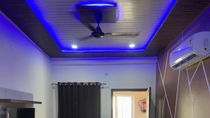 Een slaapkamer met een bed, een plafondventilator, een airconditioning, een televisie en een raam met gordijnen.