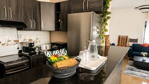 Una cocina moderna con armarios oscuros, un refrigerador de acero inoxidable, una cafetera y un tazón de bocadillos.