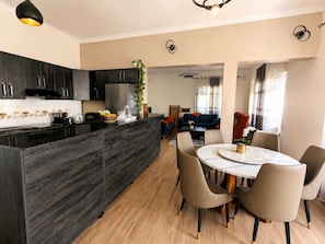 A modern kitchen with dark cabinets, a central island, and a dining area with a round table and chairs.