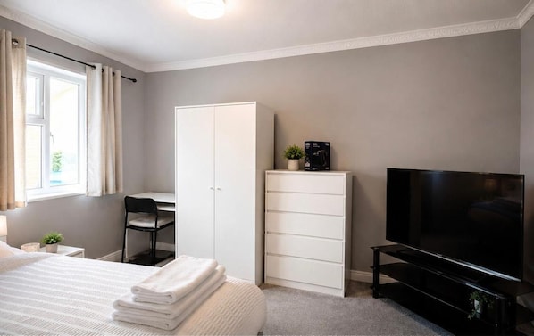 A bedroom with a bed, a desk, a wardrobe, a TV, and a small plant. - Spacious 3-bed Family Home (Sittingbourne)