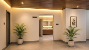A hallway with a sign indicating a washroom, potted plants, and a glimpse of a bathroom with a sink and mirror.