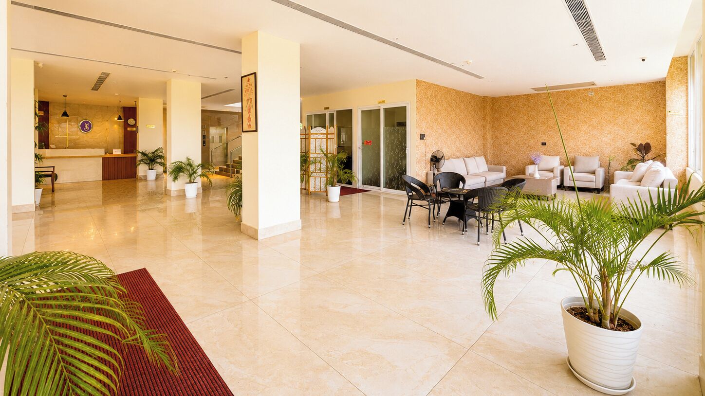 A spacious lobby with a reception desk, seating area, and potted plants.