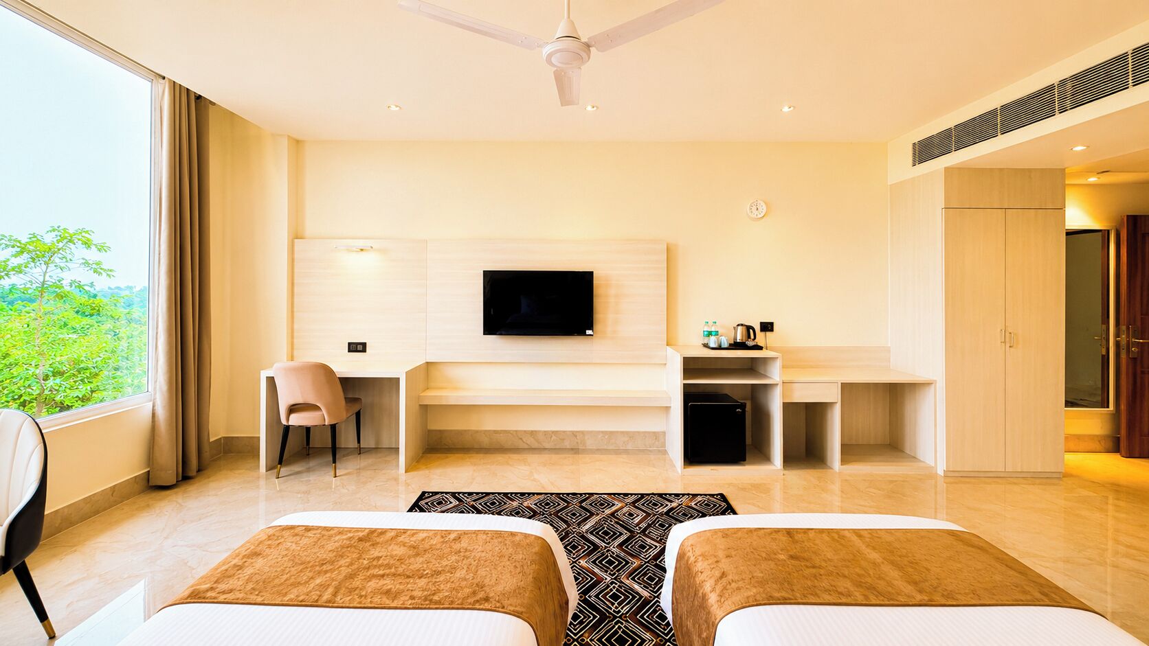 Een moderne hotelkamer met een flatscreen televisie, een bureau met stoel, een minibar en een kledingkast.
