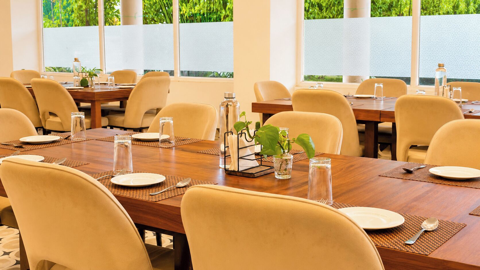 A conference room with multiple tables, chairs, and a view of greenery outside.