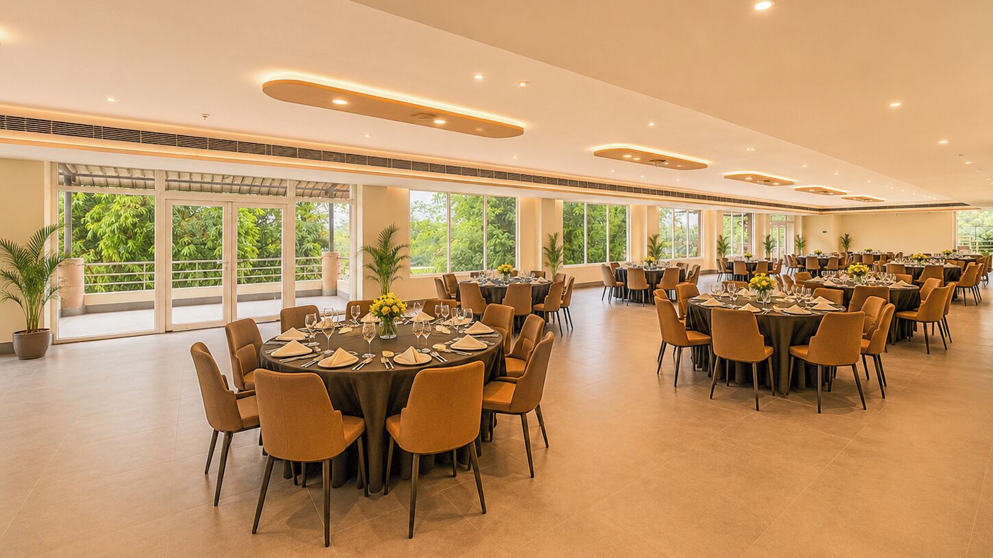 A spacious indoor dining area with multiple round tables, chairs, and potted plants.
