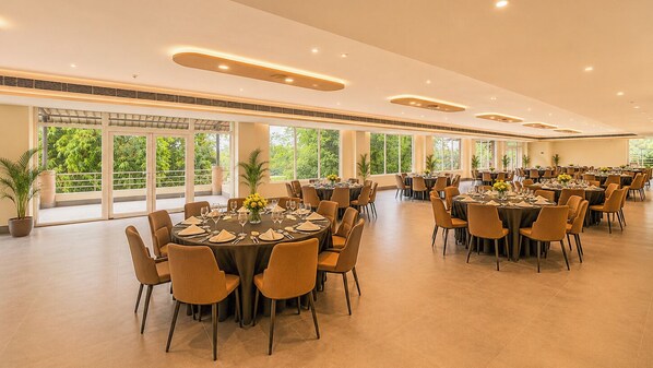 A spacious indoor dining area with multiple round tables, chairs, and potted plants. - Yashshree Namdang Premier Hotel & Banquet (Margherita)