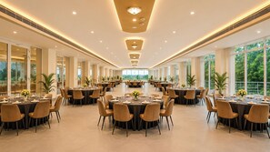 A spacious banquet hall with round tables, chairs, and large windows offering a view of the outdoors. - Yashshree Namdang Premier Hotel & Banquet (Margherita)