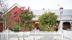Une maison en briques avec une clôture en bois peinte en blanc, un porche et des arbres en fleurs.