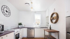 Une cuisine moderne avec des meubles blancs, des appareils en acier inoxydable, un plan de travail en bois et une étagère ronde en bois.