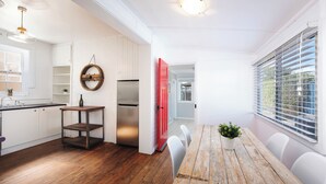 Une cuisine moderne avec des meubles blancs, une table à manger en bois et une porte rouge donnant sur une autre pièce.