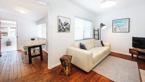 Un salon avec un plancher en bois, des murs blancs, un canapé blanc, une table basse et un meuble pour la télévision.