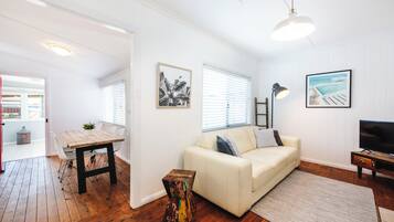Ein Wohnzimmer mit Holzboden, weißen Wänden, einem weißen Sofa, einem Couchtisch und einem TV-Schrank.