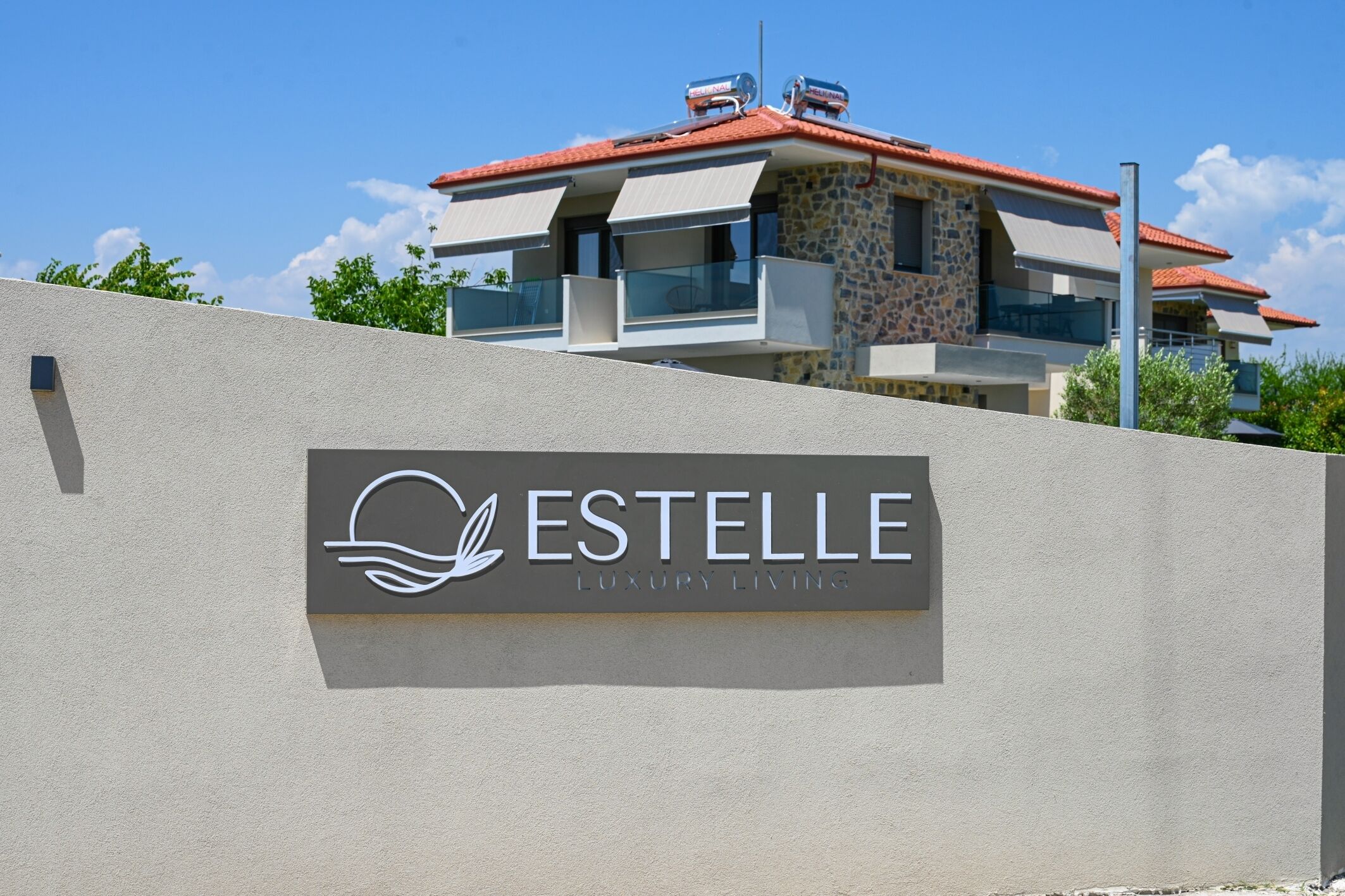 A luxury living sign for ESTELLE on a building with a red-tiled roof and stone facade.