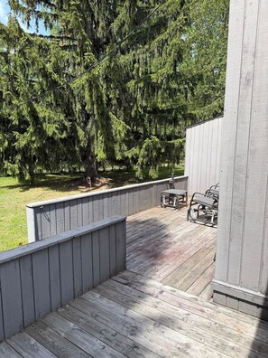 Eine Holzterrasse mit Metallstühlen, eine Betonwand und ein großer Baum im Hintergrund.